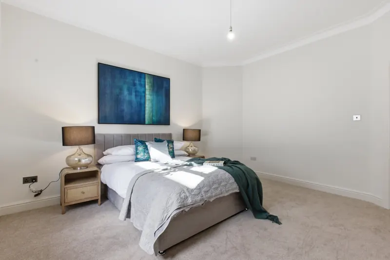 Staged bedroom with dressed double bed, glass lamps and blue artwork