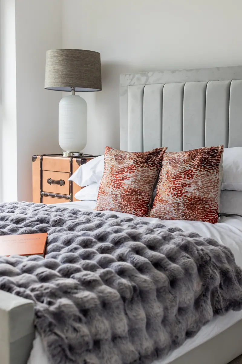 Close-up of a dressed bed with patterned cushions and grey throw