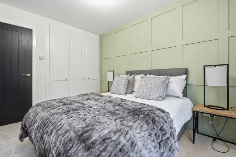 Staged bedroom with green panelled wall and grey throw